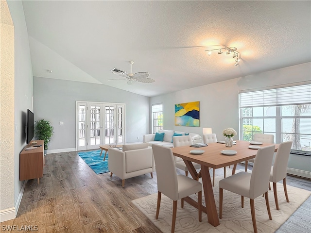 dining area featuring a textured ceiling, vaulted ceiling, wood-type flooring, french doors, and ceiling fan