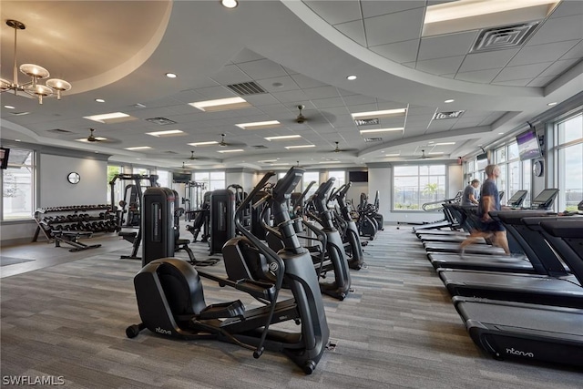 exercise room featuring a paneled ceiling, carpet flooring, and ceiling fan with notable chandelier