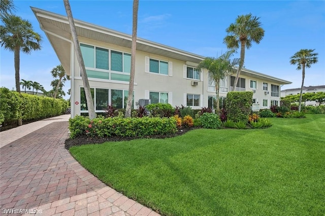 rear view of house with decorative driveway, a lawn, and stucco siding