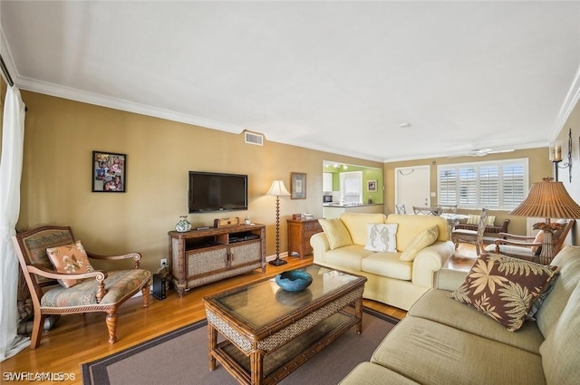 living room with wood finished floors, visible vents, and crown molding