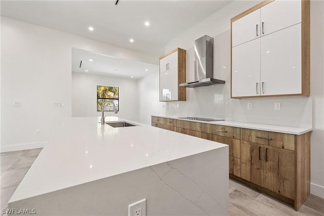 kitchen with black electric stovetop, sink, wall chimney range hood, white cabinetry, and an island with sink