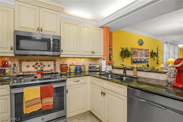 kitchen with stainless steel appliances, dark stone counters, decorative backsplash, sink, and cream cabinets