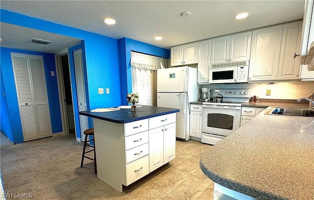 kitchen with white appliances, a kitchen island, a sink, white cabinetry, and a kitchen breakfast bar