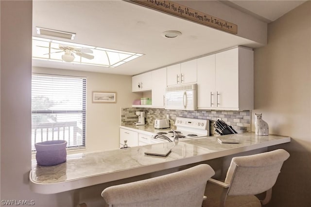 kitchen featuring a breakfast bar area, backsplash, white cabinets, and white appliances