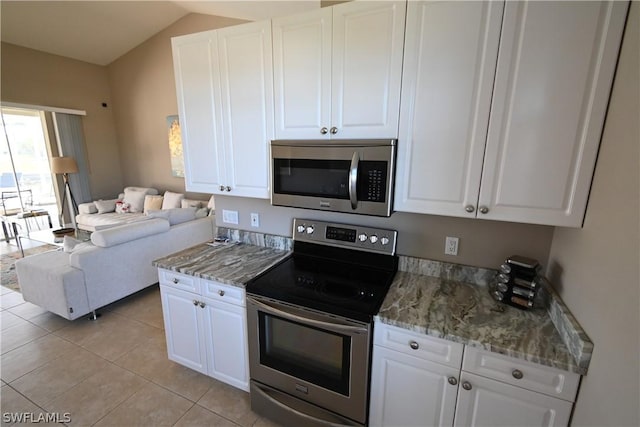 kitchen featuring appliances with stainless steel finishes, light stone counters, white cabinets, light tile patterned flooring, and vaulted ceiling