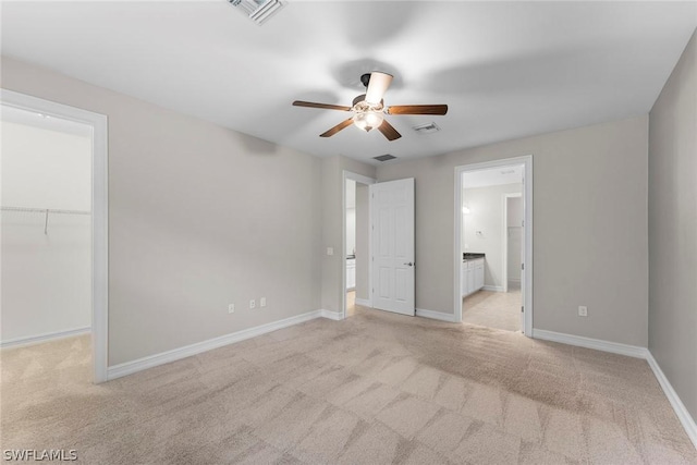 unfurnished bedroom with ensuite bathroom, a walk in closet, light carpet, a closet, and ceiling fan