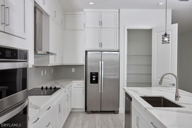 kitchen featuring decorative light fixtures, stainless steel appliances, white cabinetry, and wall chimney range hood