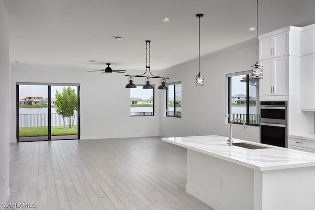 kitchen with white cabinetry, sink, ceiling fan, light stone countertops, and light hardwood / wood-style floors