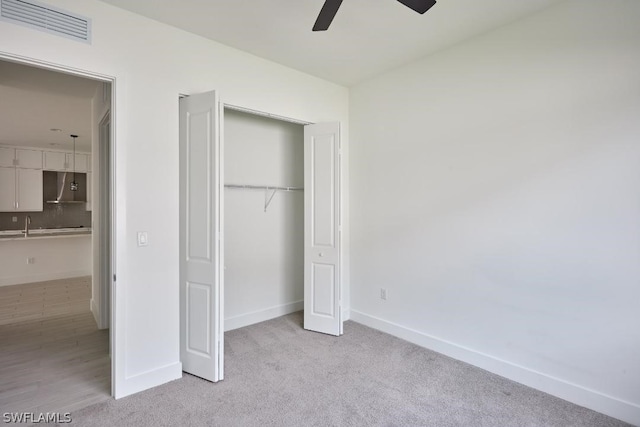 unfurnished bedroom featuring ceiling fan, a closet, light carpet, and sink