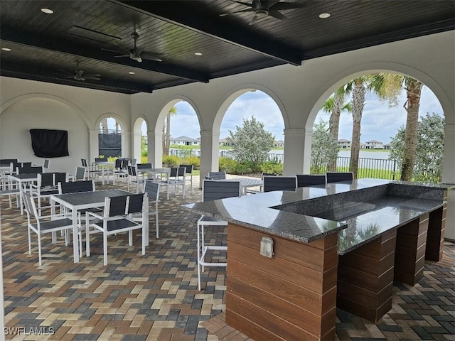 view of patio with a water view, ceiling fan, and a bar