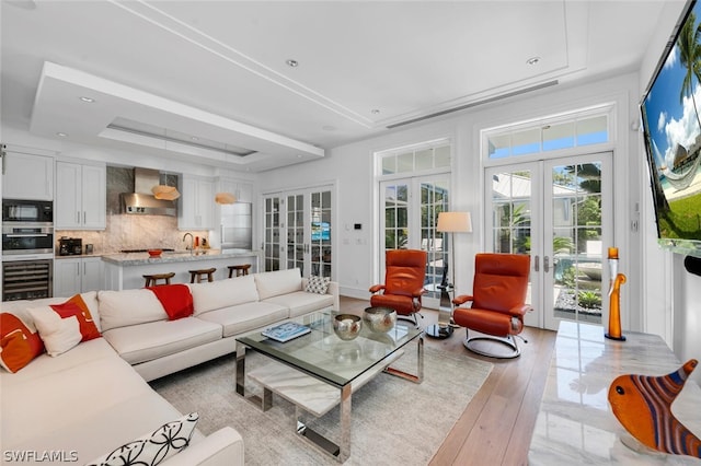 living room featuring a raised ceiling, beverage cooler, light hardwood / wood-style floors, and french doors