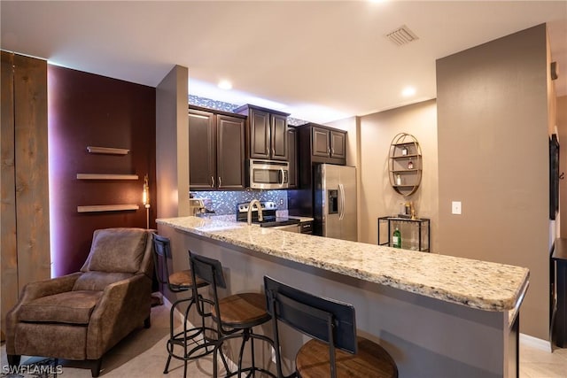 kitchen featuring backsplash, a kitchen breakfast bar, dark brown cabinets, kitchen peninsula, and stainless steel appliances