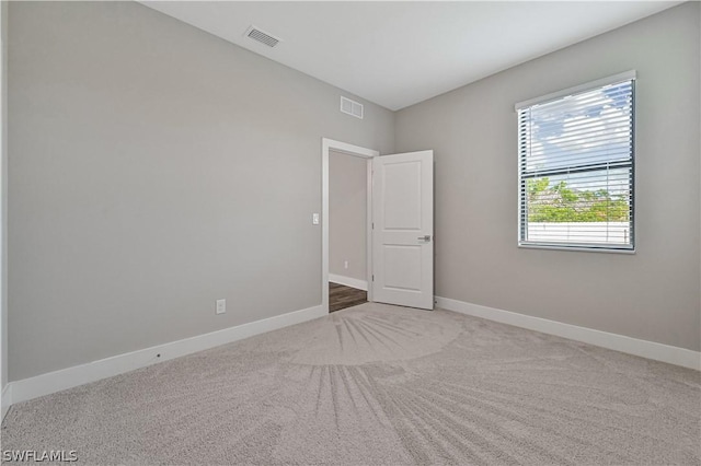 empty room featuring light carpet, visible vents, and baseboards