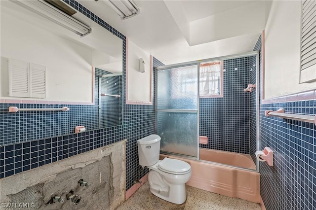 bathroom with toilet, bath / shower combo with glass door, and tile walls