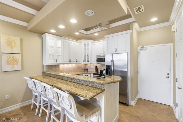 kitchen featuring kitchen peninsula, a breakfast bar area, ceiling fan, white cabinetry, and stainless steel appliances