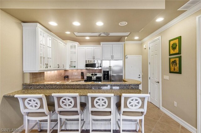 kitchen featuring kitchen peninsula, appliances with stainless steel finishes, a kitchen bar, tasteful backsplash, and white cabinetry