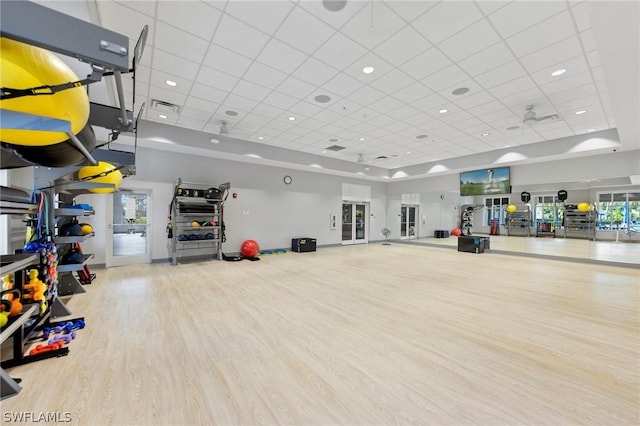 exercise area featuring a paneled ceiling, light wood-type flooring, and a towering ceiling