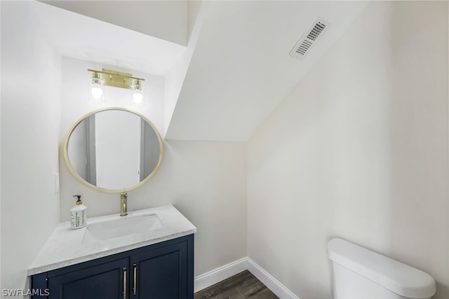 half bath featuring visible vents, baseboards, toilet, wood finished floors, and vanity