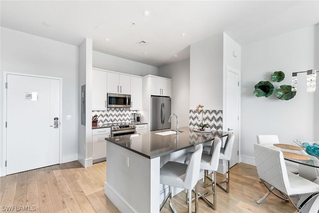 kitchen with a kitchen breakfast bar, appliances with stainless steel finishes, light wood-type flooring, sink, and white cabinetry