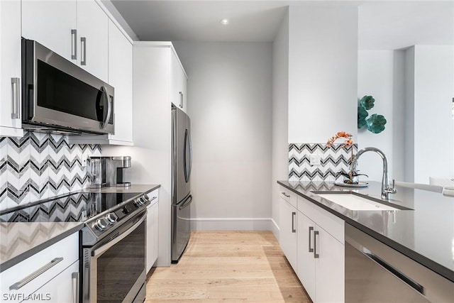 kitchen with stainless steel appliances, white cabinetry, sink, and dark stone counters