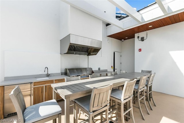 kitchen with a high ceiling, light colored carpet, a skylight, custom range hood, and sink