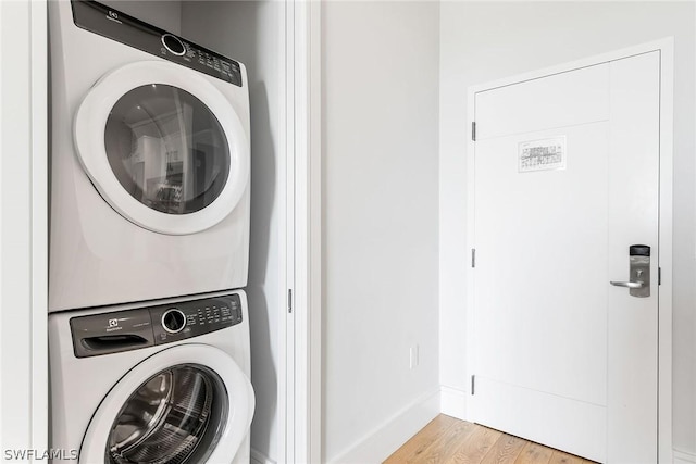 laundry room with light wood-type flooring and stacked washer / drying machine