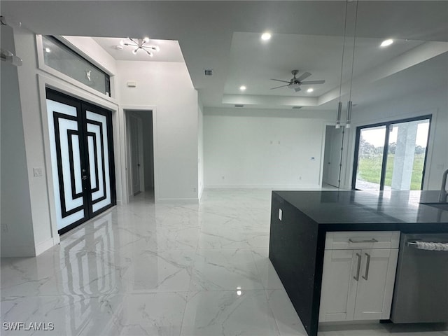 kitchen featuring white cabinetry, stainless steel dishwasher, a tray ceiling, ceiling fan with notable chandelier, and sink