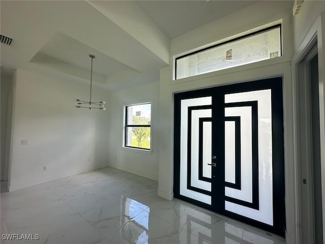 foyer featuring french doors, a tray ceiling, and an inviting chandelier