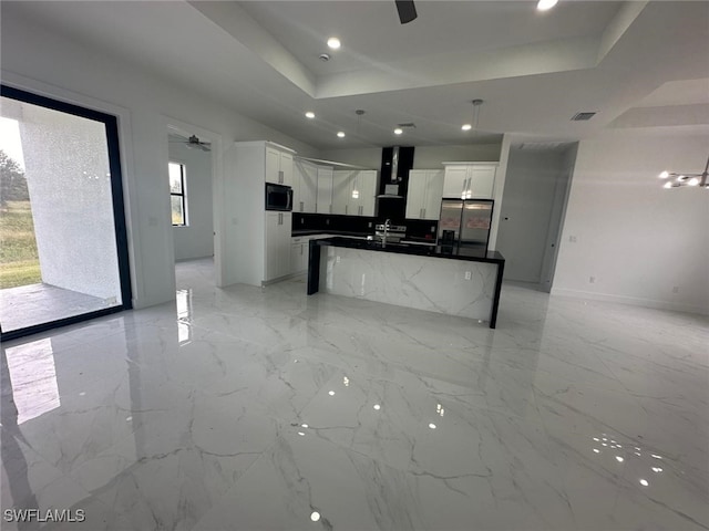 kitchen with white cabinetry, ceiling fan, wall chimney exhaust hood, a kitchen island with sink, and stainless steel refrigerator with ice dispenser