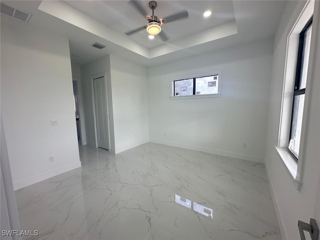 unfurnished room featuring a tray ceiling, plenty of natural light, and ceiling fan