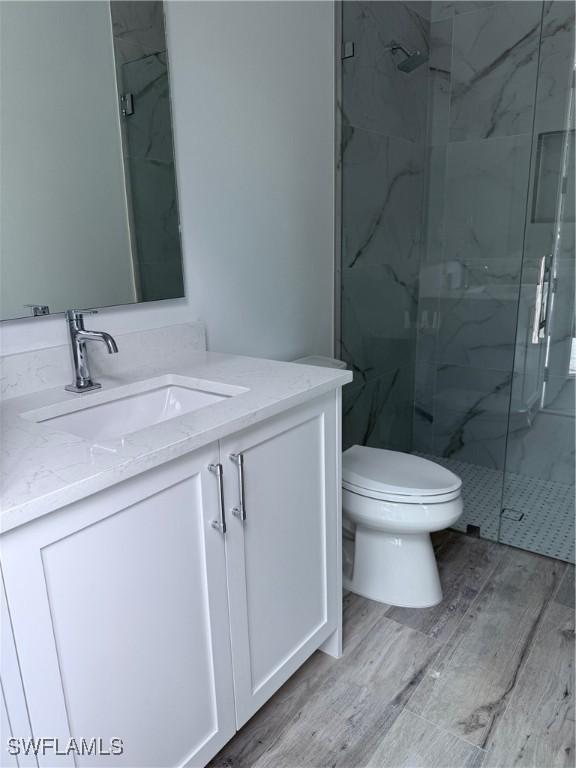 full bathroom with a marble finish shower, vanity, and wood finished floors