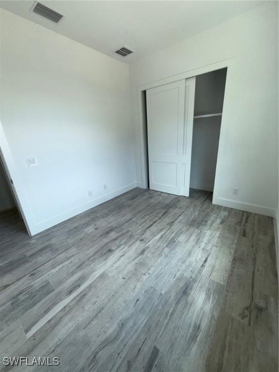 unfurnished bedroom featuring baseboards, a closet, wood finished floors, and visible vents