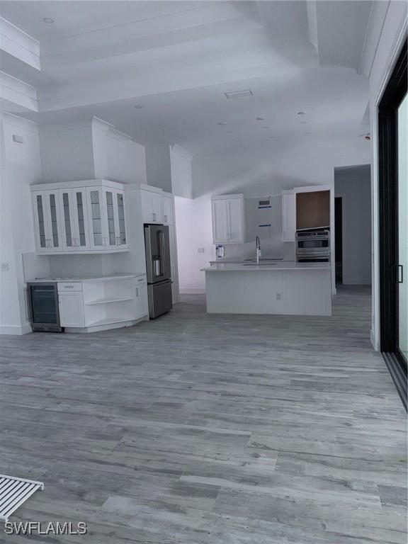 unfurnished living room featuring baseboards, a sink, light wood finished floors, and wine cooler