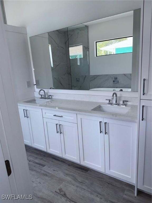 bathroom featuring double vanity, a marble finish shower, and a sink