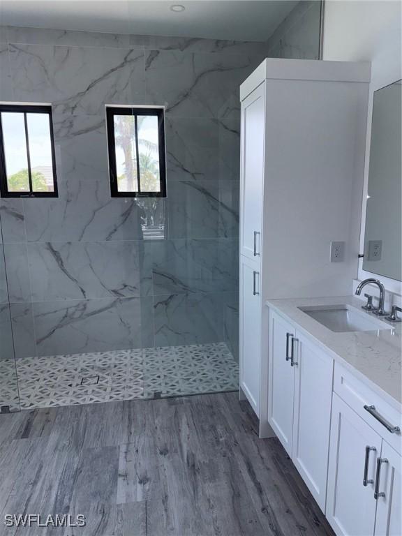 full bath featuring wood finished floors, a marble finish shower, and vanity