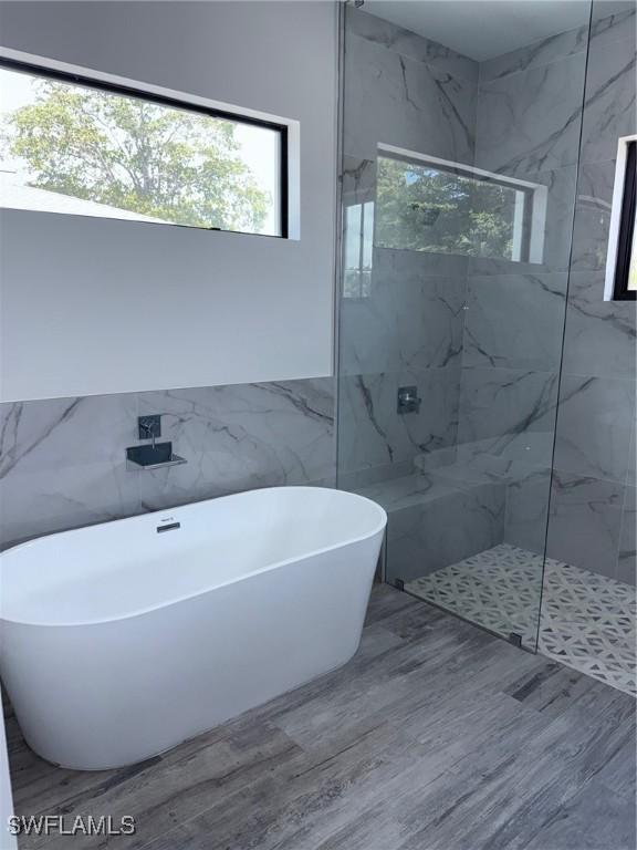 bathroom with a marble finish shower, a soaking tub, a healthy amount of sunlight, and tile walls