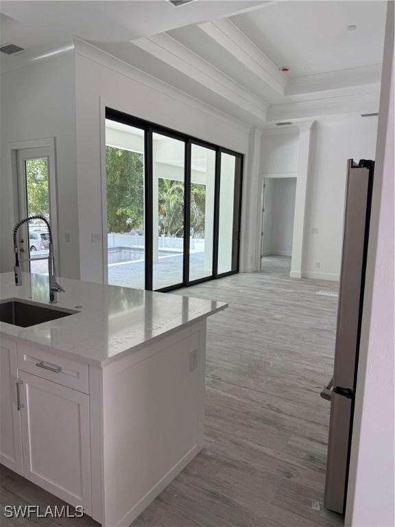 kitchen with visible vents, a sink, white cabinets, freestanding refrigerator, and ornamental molding