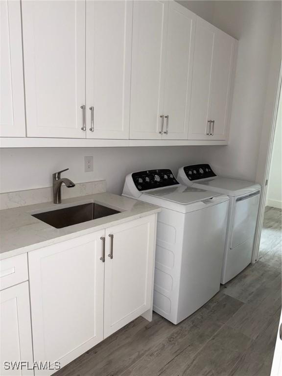 laundry area featuring a sink, washer and clothes dryer, cabinet space, and light wood-style flooring