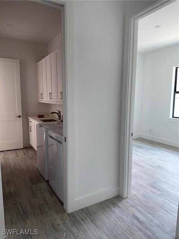 clothes washing area featuring washing machine and clothes dryer, cabinet space, a sink, baseboards, and light wood-style flooring