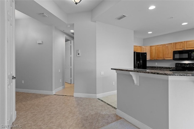 kitchen with light brown cabinetry, a breakfast bar, light tile patterned flooring, and black appliances