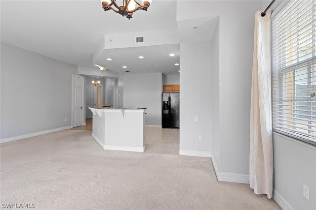 kitchen with light carpet, stone counters, black fridge, a notable chandelier, and a breakfast bar area