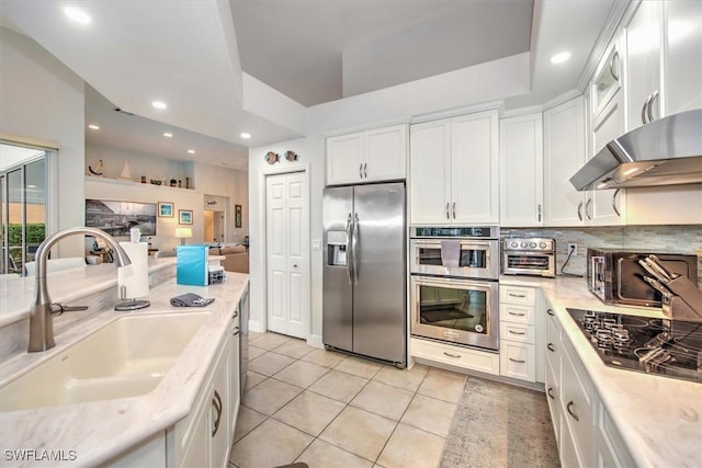 kitchen featuring wall chimney exhaust hood, sink, white cabinetry, light tile patterned floors, and appliances with stainless steel finishes