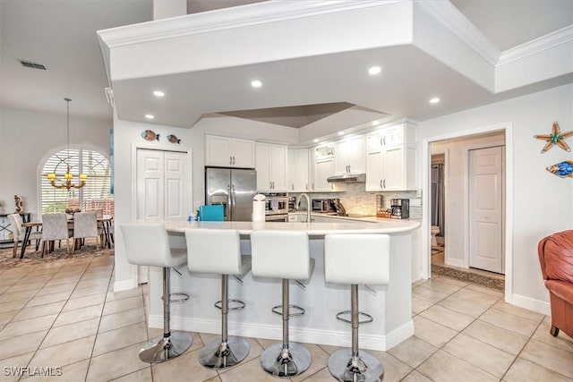 kitchen with white cabinets, stainless steel fridge, a kitchen bar, light tile patterned floors, and crown molding