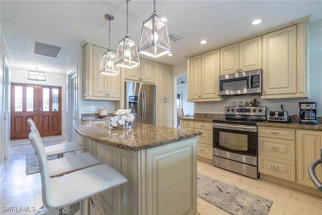 kitchen featuring a kitchen island, a kitchen breakfast bar, hanging light fixtures, stainless steel appliances, and cream cabinets