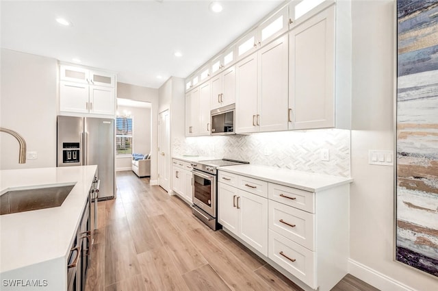 kitchen featuring sink, light hardwood / wood-style flooring, backsplash, white cabinetry, and appliances with stainless steel finishes