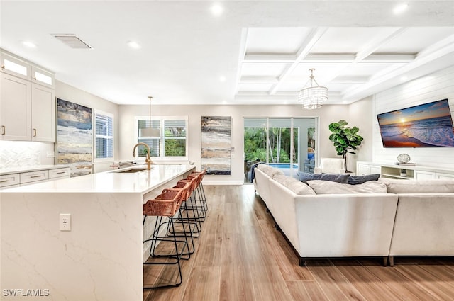 living room featuring light hardwood / wood-style floors, sink, a notable chandelier, beam ceiling, and coffered ceiling