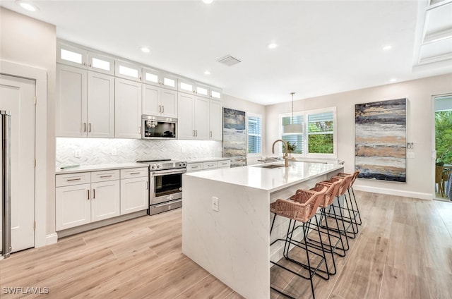 kitchen with an island with sink, stainless steel appliances, sink, and white cabinetry