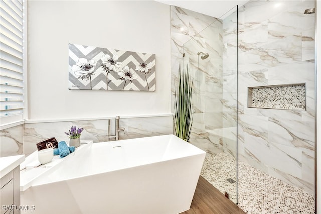 full bath featuring a freestanding tub, wood finished floors, vanity, tile walls, and a marble finish shower