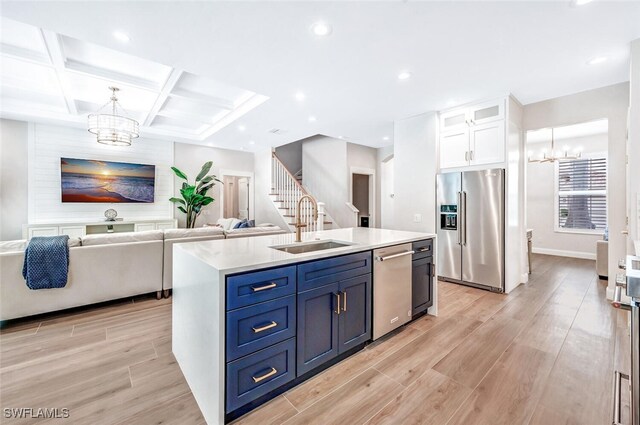 kitchen featuring an inviting chandelier, stainless steel appliances, white cabinetry, and a kitchen island with sink