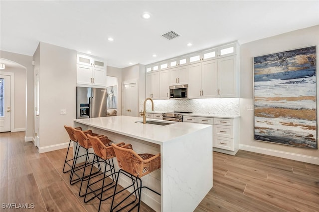 kitchen featuring an island with sink, white cabinets, light hardwood / wood-style floors, and appliances with stainless steel finishes